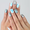 Hand model showing short coffin-shaped blue press-on nails with glossy metallic silver and 3D water droplet textures