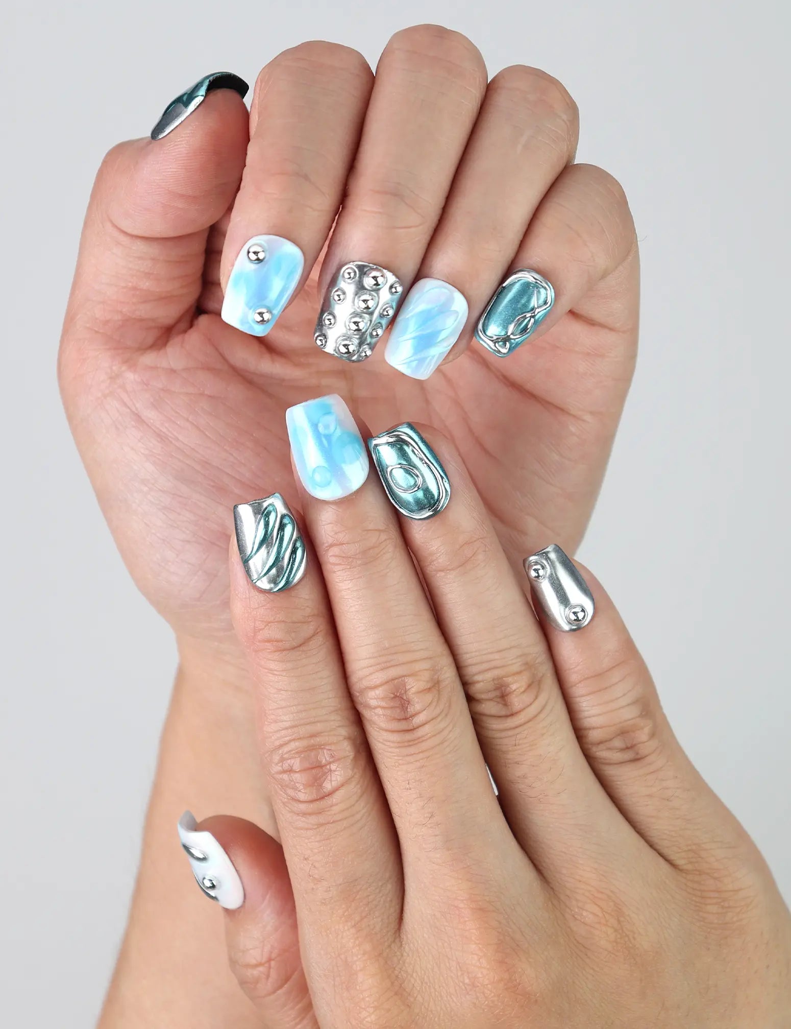 Close-up of Naillover’s short coffin nails in deep blue with reflective silver sheen and raised water drop designs