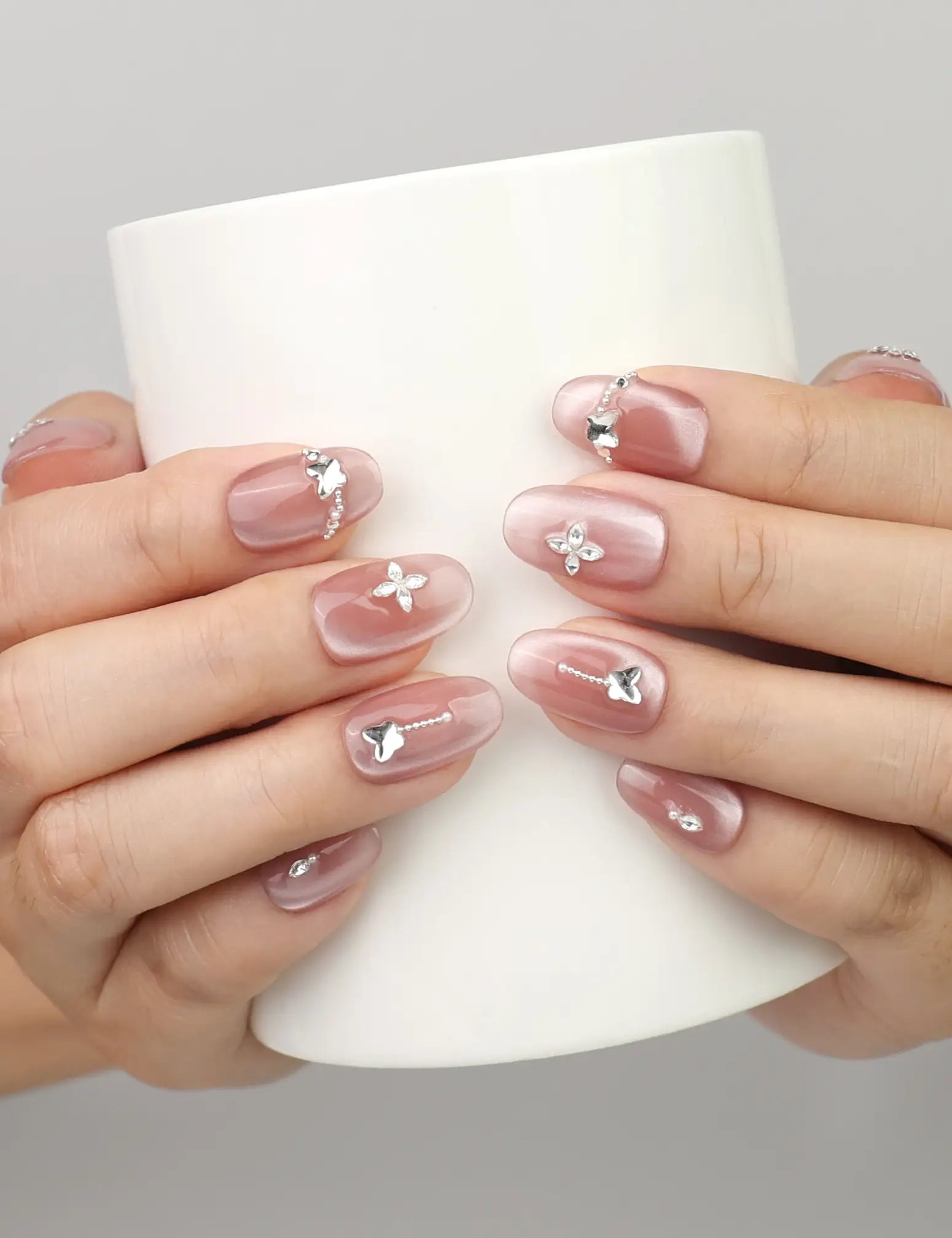 Hand holding a cup while wearing Naillover Silver Charm handmade press on nails with glossy cat eye finish and butterfly accents.