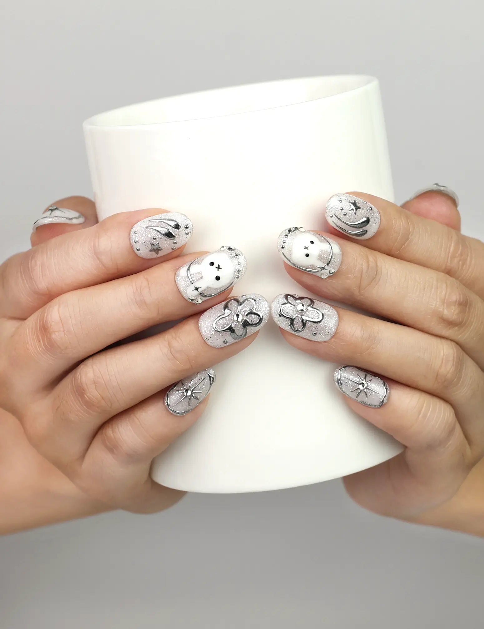 Hand holding a cup while wearing Naillover Silver Starry Cutie handmade press on nails with whimsical bunny and star designs.