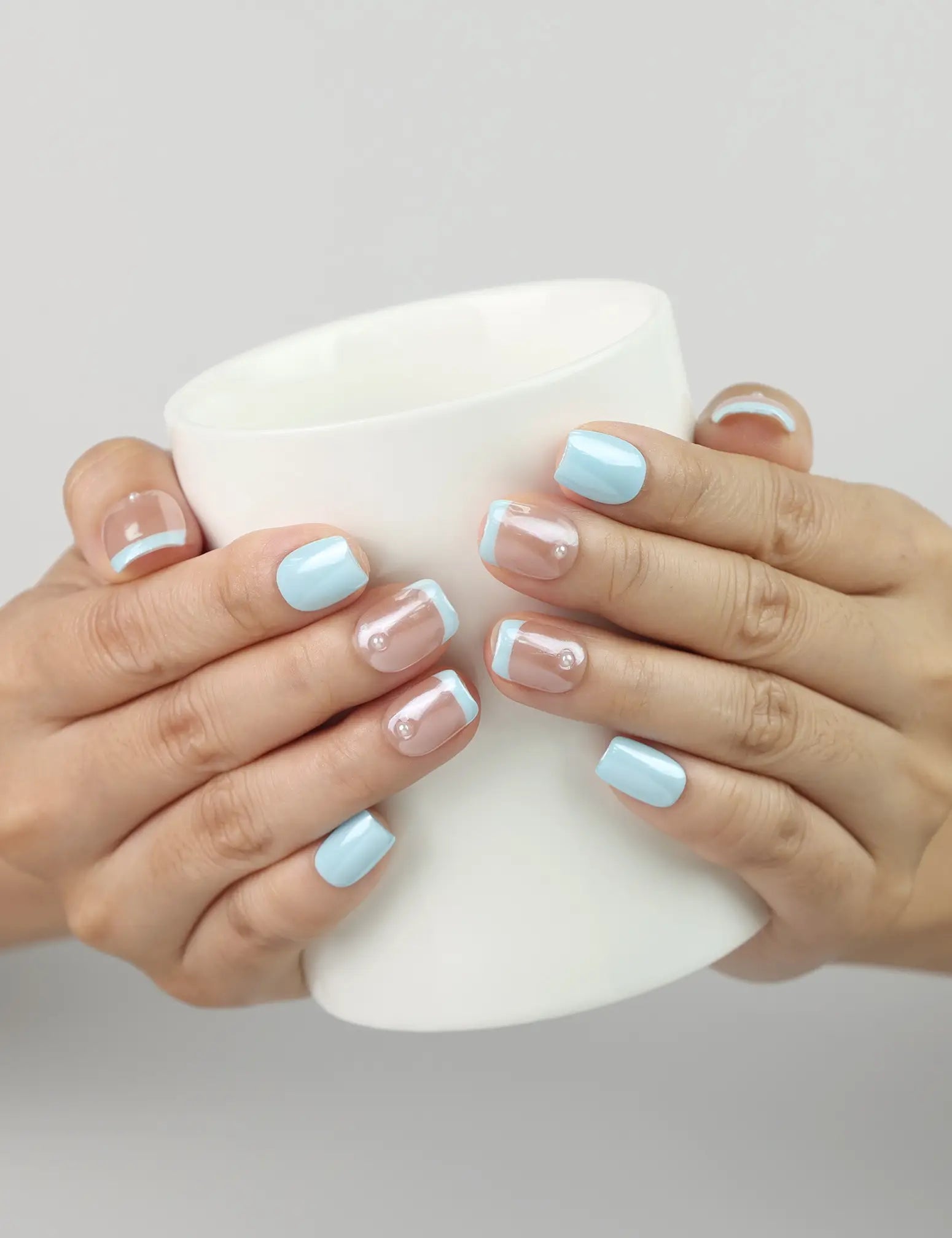 Model holding a coffee cup wearing Skyline ombre blue handmade press on nails, Singapore style gradient design