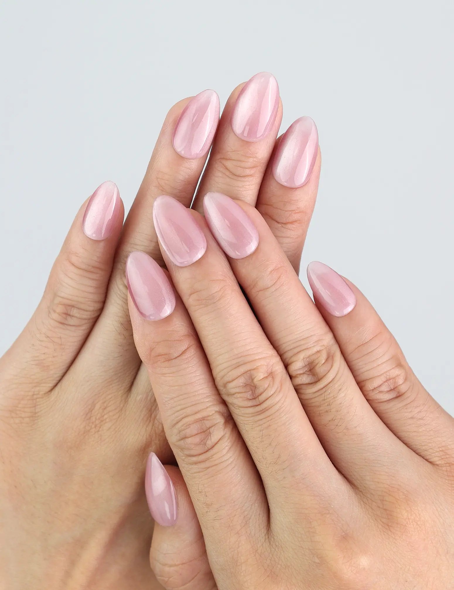 Hand wearing Naillover Soft Mirage press on nails with pink cat eye shimmer in almond shape.