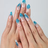 Hand wearing blue gradient almond press-on nails with shell-like texture and sparkling glitter, inspired by ocean beauty