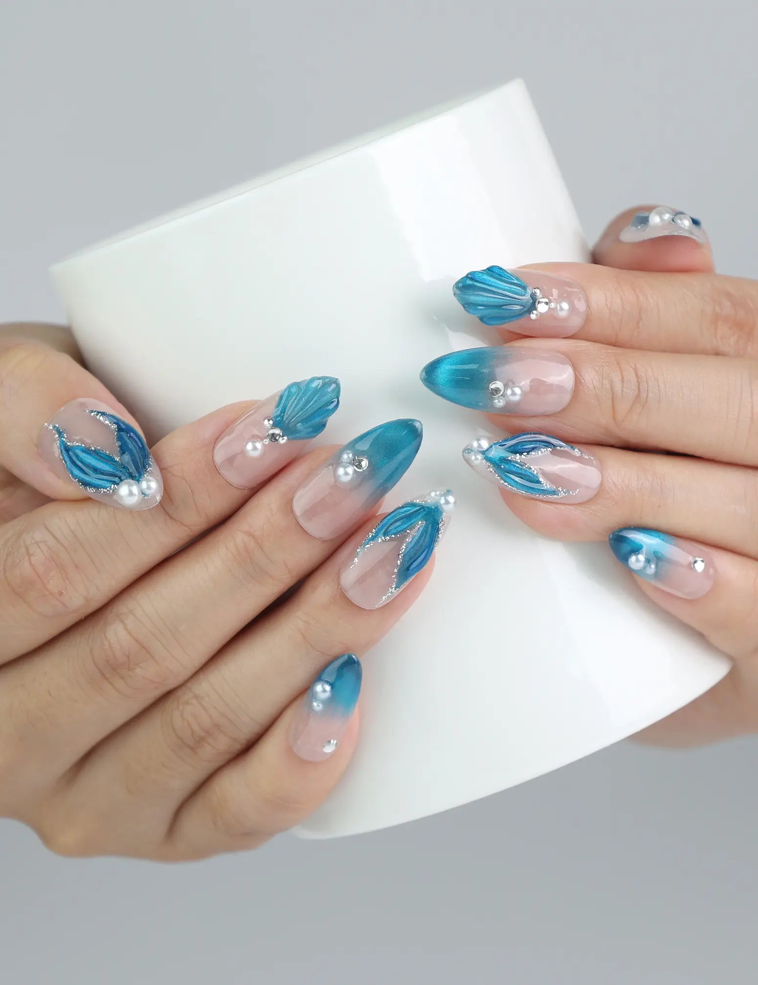 Hand holding a cup, showcasing Naillover mermaid-style press-on nails with pastel blue gradients and ocean textures