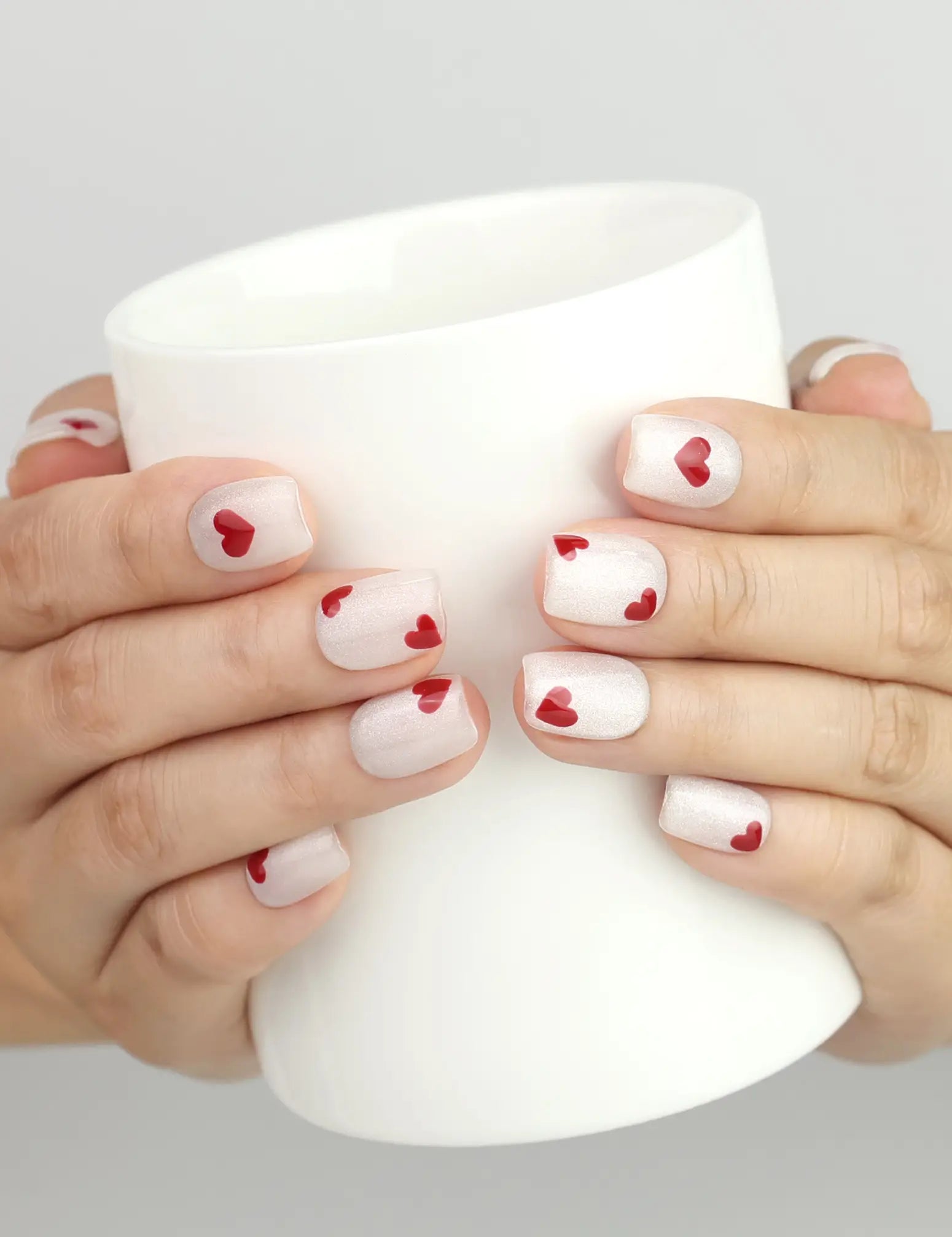Hand holding a cup while wearing naillover Sparkle Love Singapore press on nails, white glitter with red hearts, stylish handmade nails for everyday chic.