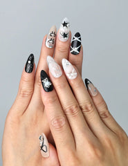 Hand model wearing nude and black almond-shaped press-on nails with tiny stars and cute bow accents