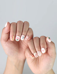 Delicate fingers posed to highlight short press on nails in pastel pink with charming strawberry and heart designs by Naillover