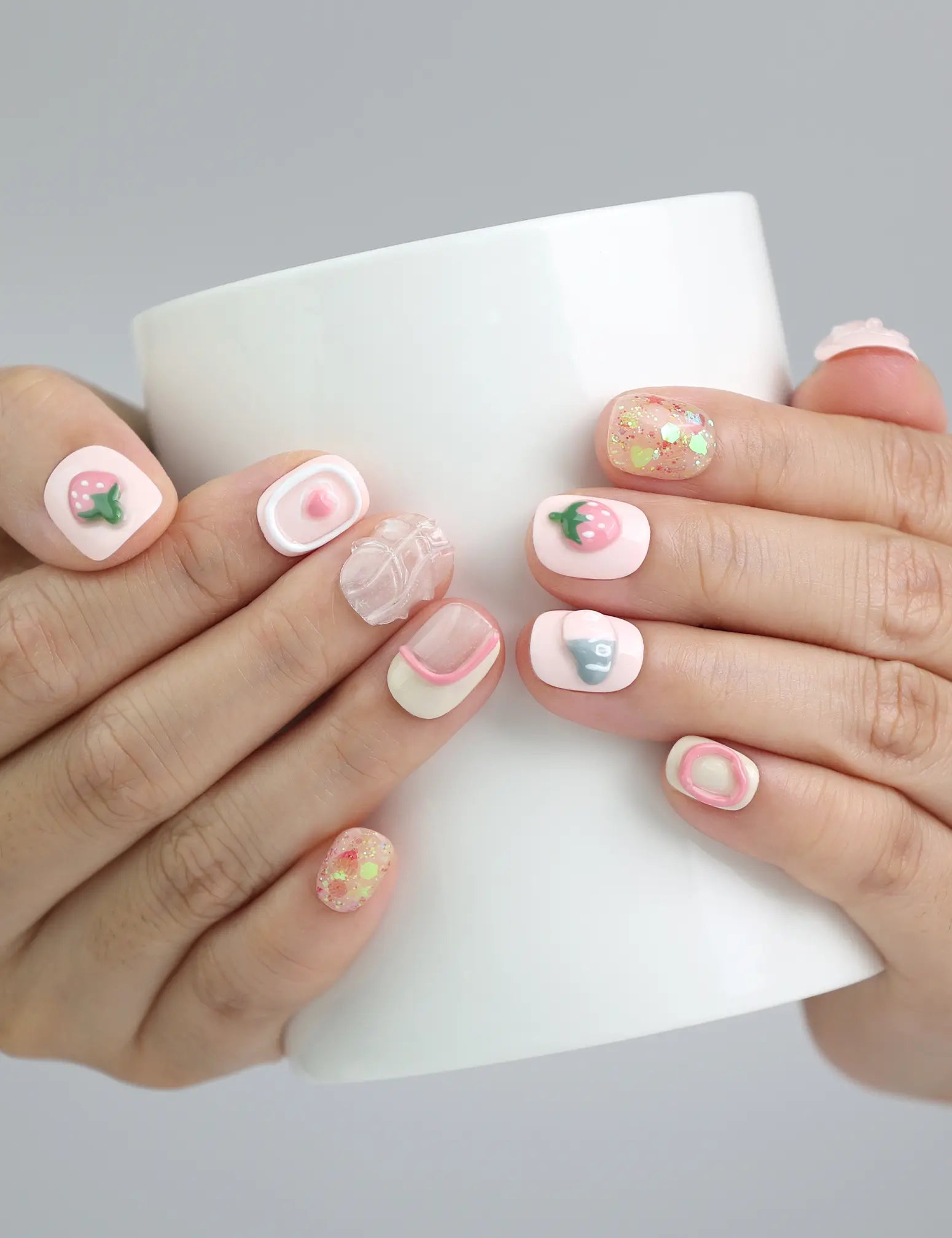 Holding a cup with soft pink press on nails adorned with strawberry and heart motifs, handmade in Singapore by Naillover