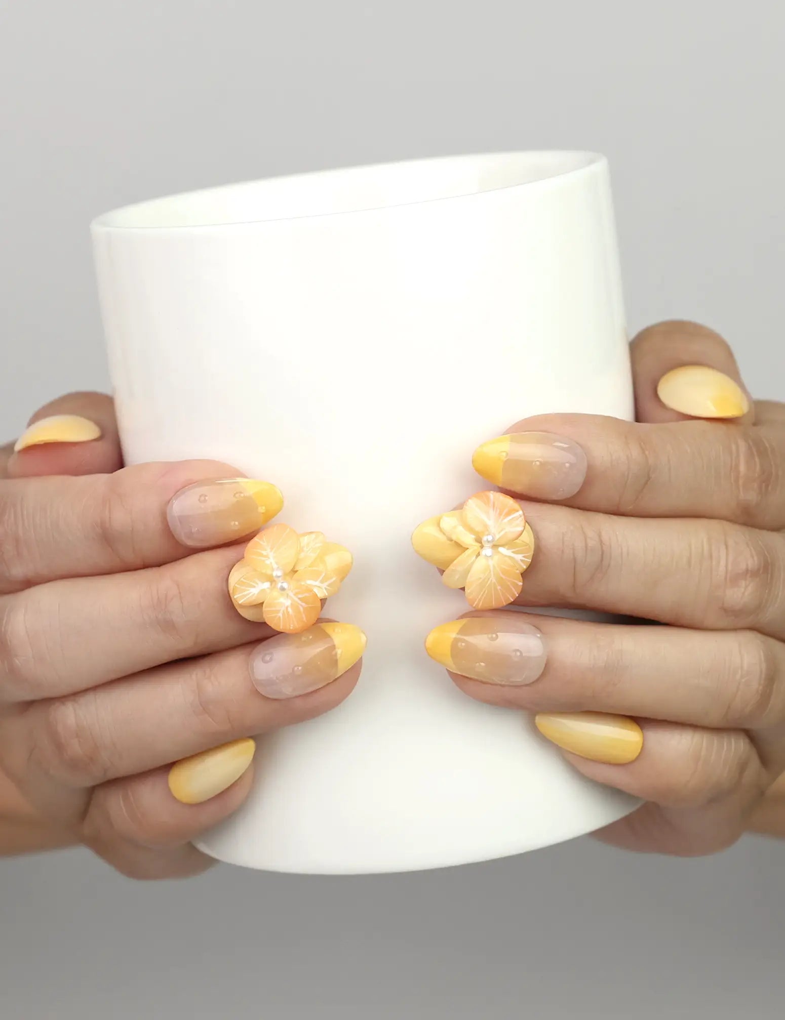 Hand holding a cup while wearing Naillover Sunny Bloom handmade press on nails with yellow gradient and 3D flower pearl charm.