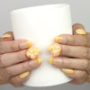 Hand holding a cup while wearing Naillover Sunny Bloom handmade press on nails with yellow gradient and 3D flower pearl charm.