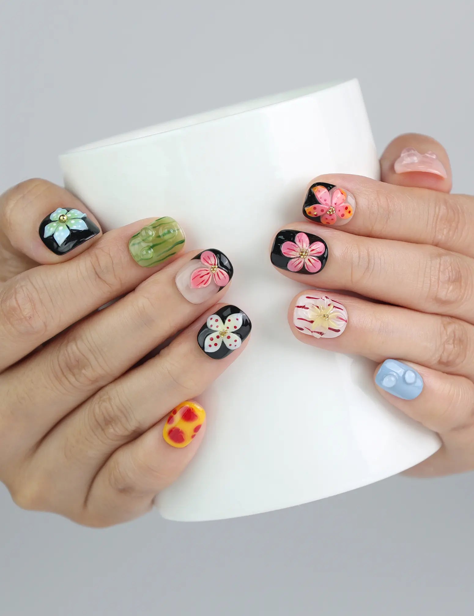 Hand holding a cup while wearing Naillover’s nude and black squoval nails adorned with 3D pink floral designs