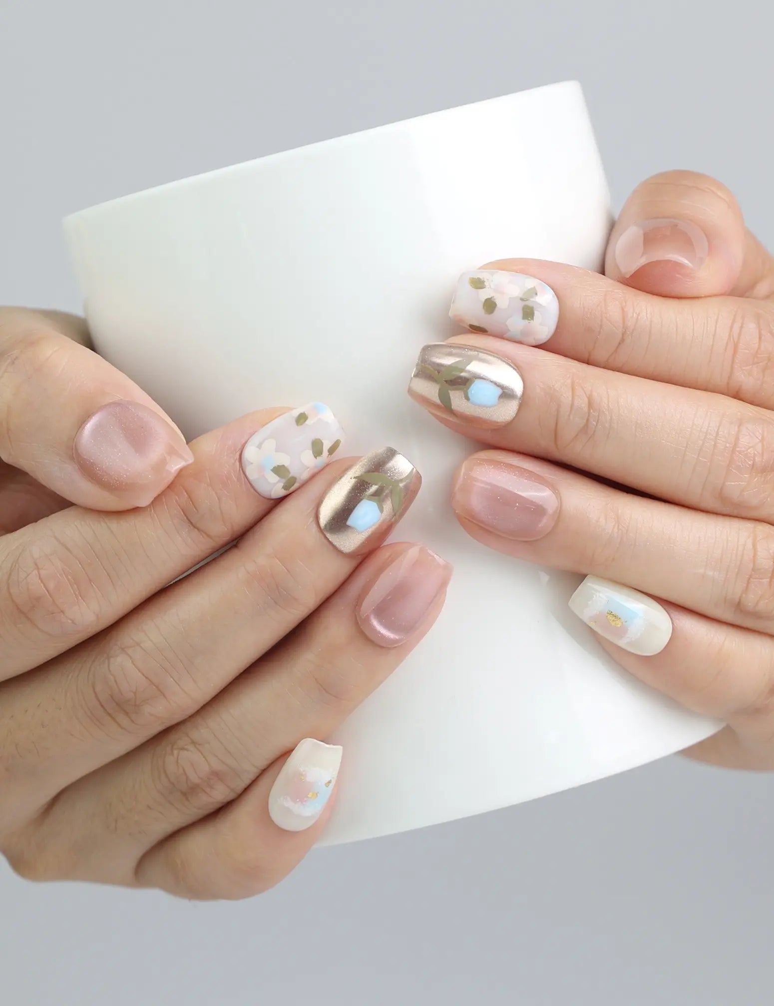 Hand holding a cup, showcasing Naillover’s short pink square nails with intricate floral art and light-reflecting shimmer