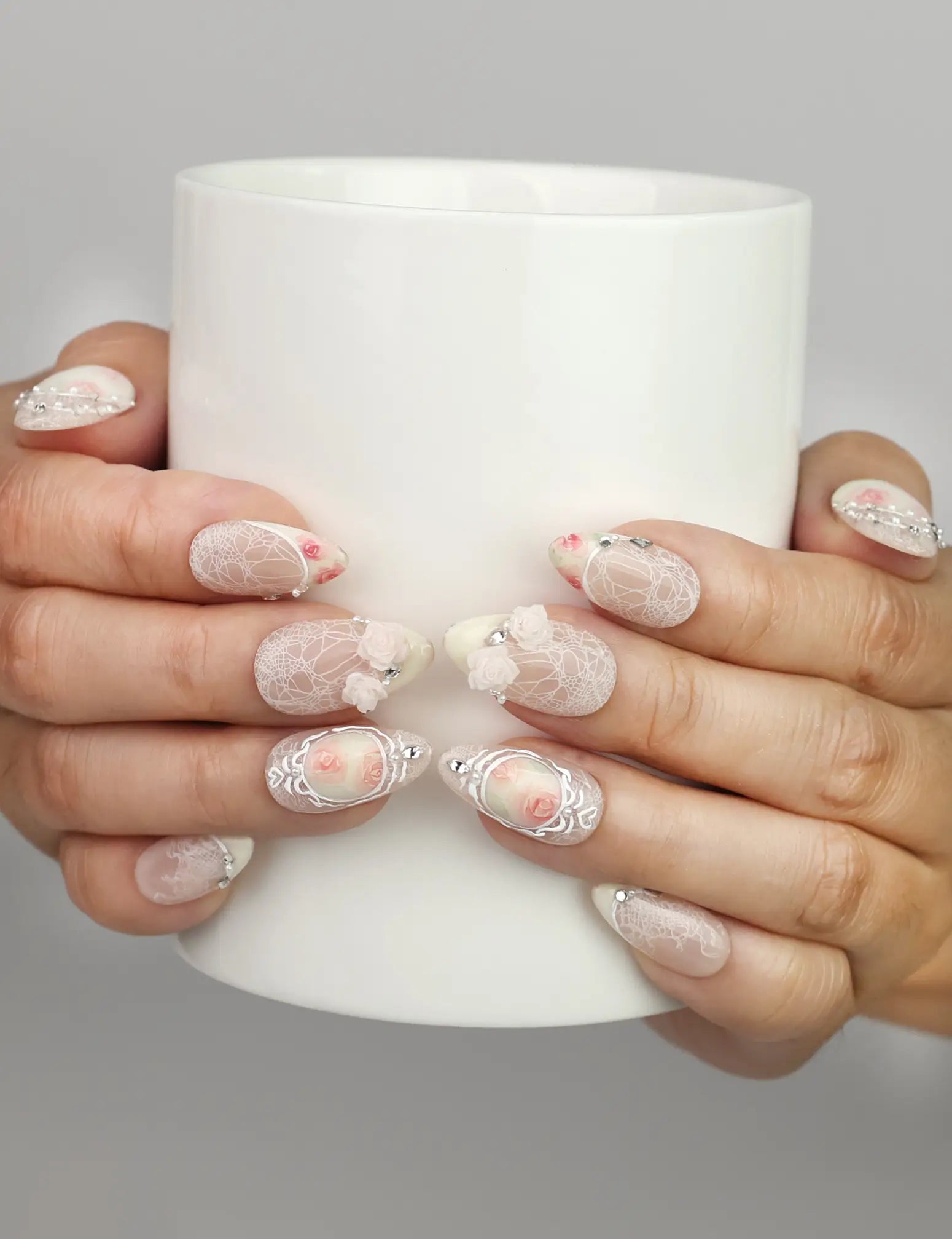 Hand holding a cup while wearing Naillover Vintage Rose Lace handmade press on nails with vintage floral and pearl details.