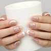 Hand holding a cup while wearing Naillover Whisper Beige handmade press on nails with sheer nude gradient and gemstone accent.