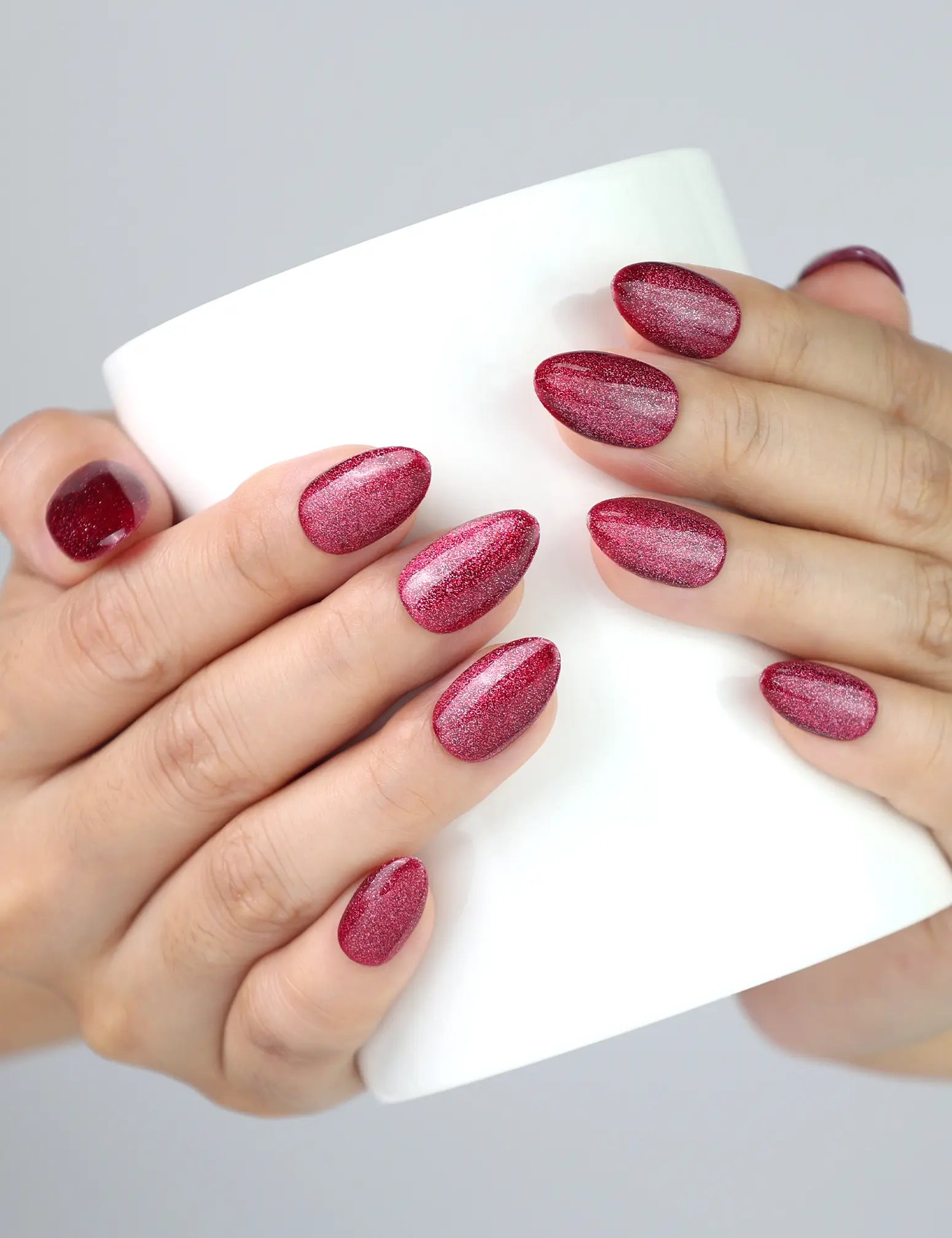 Hand holding a cup while wearing Wine Illusion press on nails, deep red cat eye almond nails by Naillover.