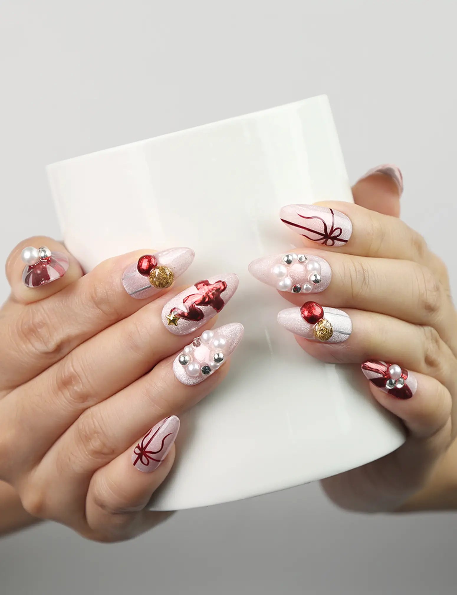 Hand holding a cup wearing Xmas Sparkle red and white handmade press-on nails with festive bows, Singapore nails by naillover